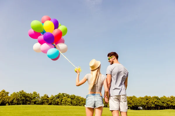 Achteraanzicht van man en vrouw met ballonnen hand in hand — Stockfoto