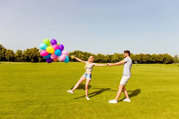 Young happy man carrying his girlfriend with balloons — Stock Photo, Image