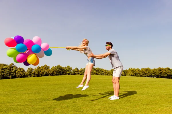 Happy man catching his girlfriend not to fly with balloons — Stock Photo, Image