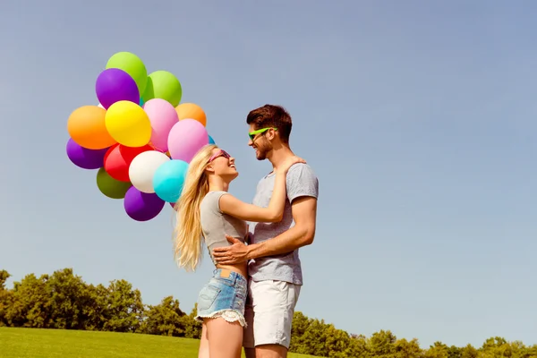 Joven hombre feliz abrazando a su chica y sosteniendo globos — Foto de Stock