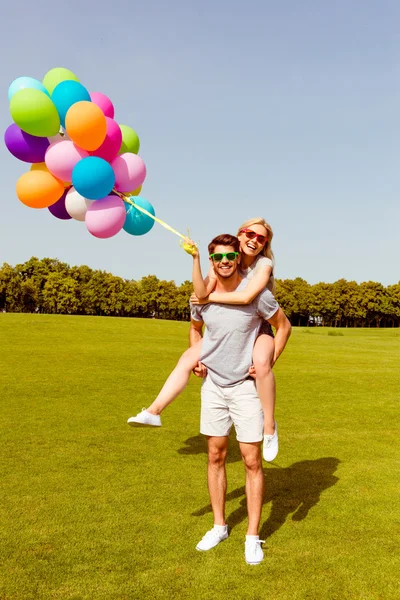 Feliz homem bonito carregando sua namorada com balões — Fotografia de Stock