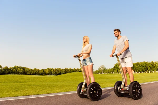 Joven pareja alegre en el amor conduciendo segways y sonriendo en pa —  Fotos de Stock