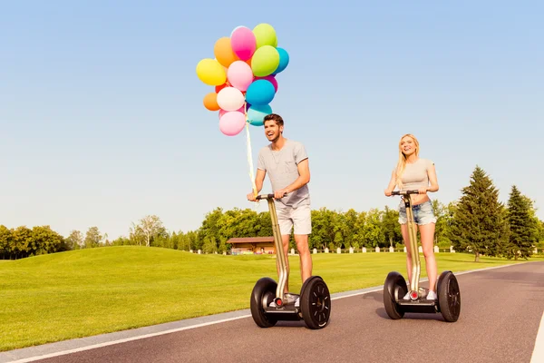 Dos amantes felices con globos teniendo tour en segway en parque —  Fotos de Stock