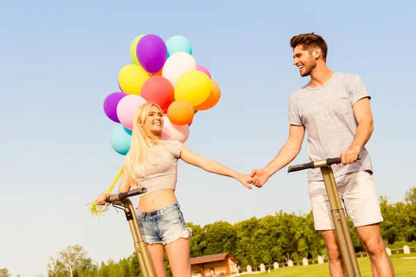 Счастливая прекрасная пара с шариками, держащимися за руки и использующими сегва — стоковое фото
