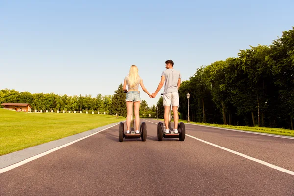 Vista posterior del hombre y la mujer tomados de la mano y montar segway —  Fotos de Stock