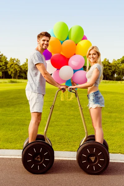 Retrato de jóvenes amantes felices con globos usando segway a la par —  Fotos de Stock