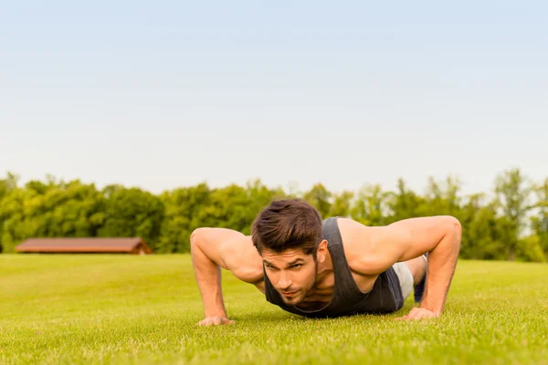 Portrait of strong young athlete push-uping in the park — Stock Photo, Image