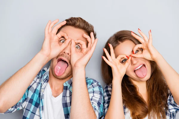 Retrato cómico de amantes divertidos mostrando lenguas y sosteniendo dedos — Foto de Stock