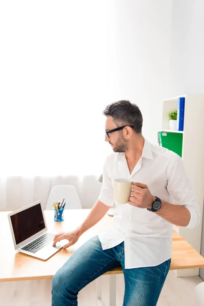 Man in glazen zittend op een tafel met laptop en koffie drinken — Stockfoto