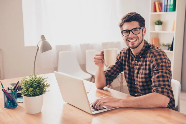 Glücklich lächelnder Mann in Brille arbeitet mit Laptop und trinkt mit — Stockfoto