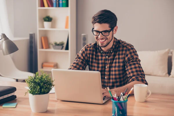 Knappe vrolijke jongeman in glazen typen op laptop — Stockfoto