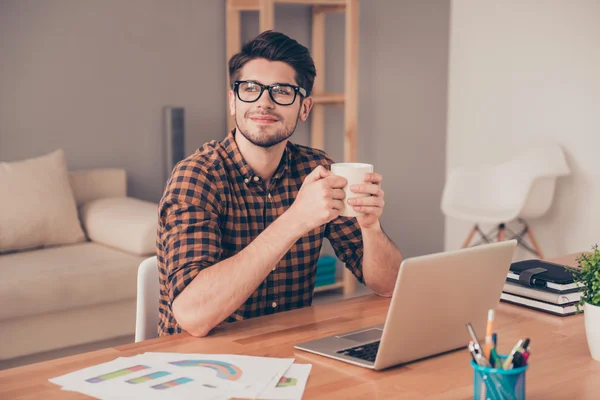 Молодой красивый мужчина в очках пьет кофе в офисе и мечтает — стоковое фото