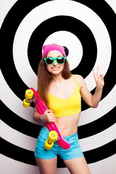 Hipster χαριτωμένο δροσερό κορίτσι σε γυαλιά κρατώντας skate και χαμογελαστός — Φωτογραφία Αρχείου