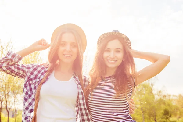 Two positive smiling girls in caps walking in the park and smil — Stock Photo, Image