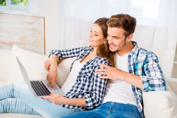 Feliz pareja joven sentado en el sofá y el uso de la computadora portátil — Foto de Stock