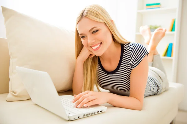 Chica bastante sonriente acostado en el sofá y el uso de ordenador portátil — Foto de Stock