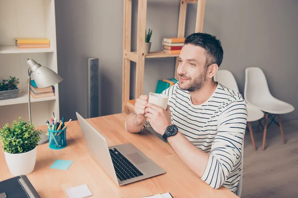 Счастливый бородатый мужчина пьет кофе в офисе и мечтает — стоковое фото