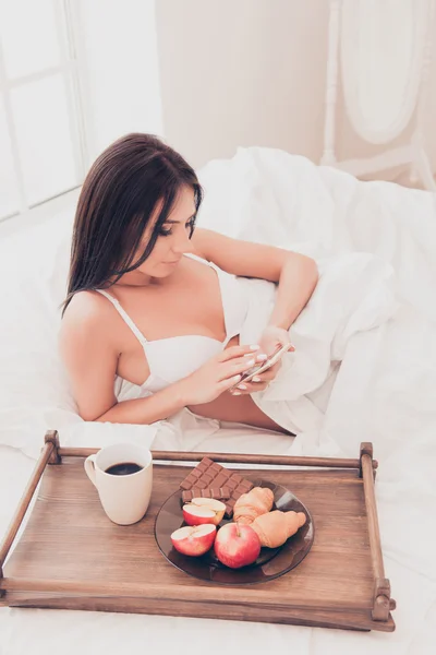 かわいい女の子のベッドで朝食をとり、メッセージを入力します。 — ストック写真