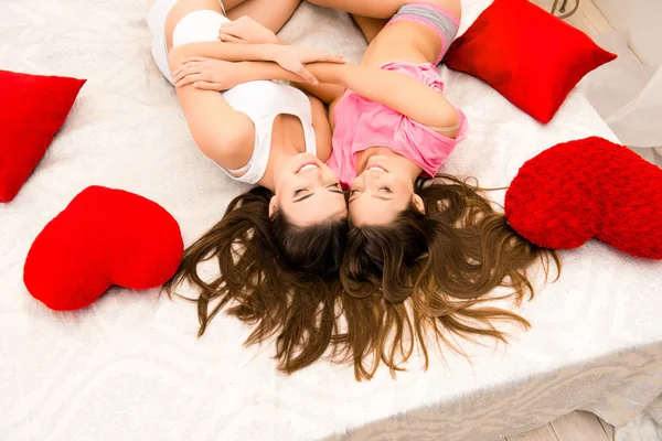 Вид смеющихся девочек в пижамах, лежащих на кровати и обнимающихся — стоковое фото