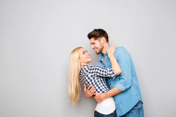 Glücklich lächelnde junge Liebende, die sich auf grauem Hintergrund umarmen — Stockfoto