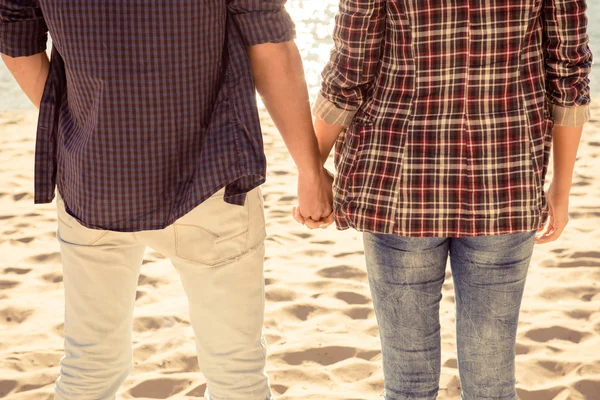 Stäng upp bakifrån av par i kärlek hand i hand på stranden — Stockfoto