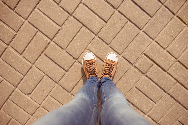 Top view of legs of girl in gumshoes and jeans on pavement — Stock Photo, Image
