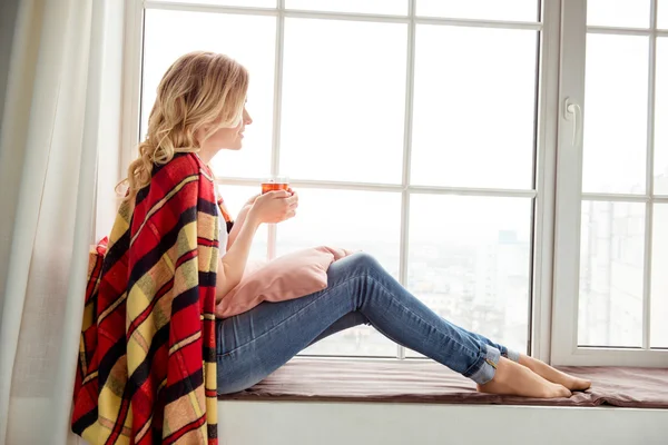 Vue latérale de la jeune femme assise sur le rebord de la fenêtre et se prélasser avec — Photo