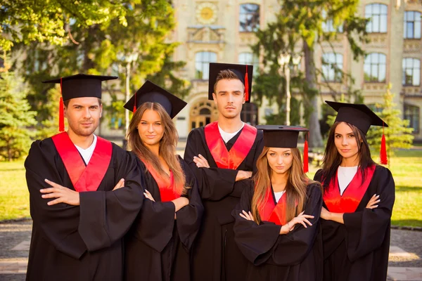 Úspěšní absolventi jistý pět v pláště a klobouky stojící i — Stock fotografie