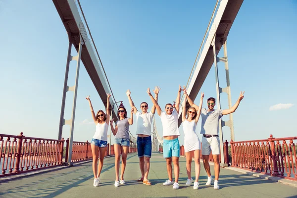 Счастливая группа бойфрендов и подружек ходят по мосту с руками — стоковое фото