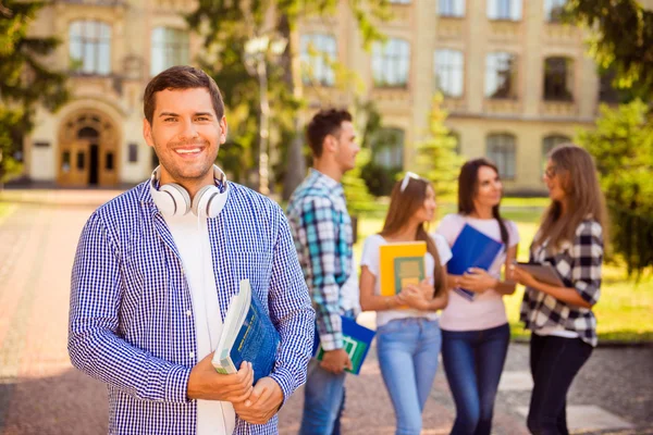 Szczęśliwy młody człowiek trzymania książek, podczas gdy stojący Uniwersytetu backgrou — Zdjęcie stockowe