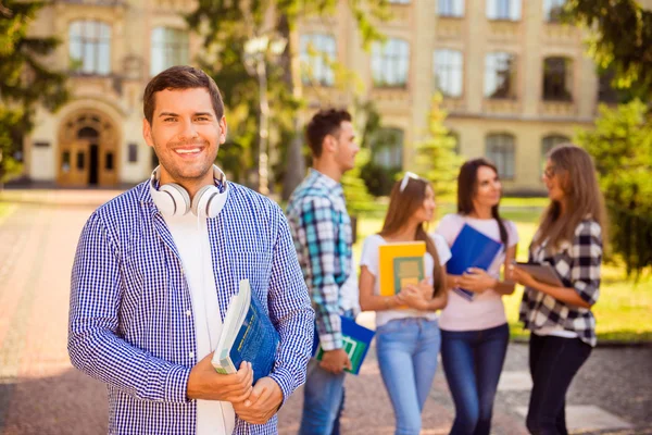 Jovem feliz segurando livros enquanto estava de pé backgrou universidade — Fotografia de Stock