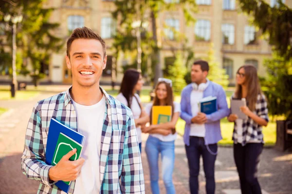 Feliz joven descanso y sosteniendo libros mientras está de pie en backgro —  Fotos de Stock