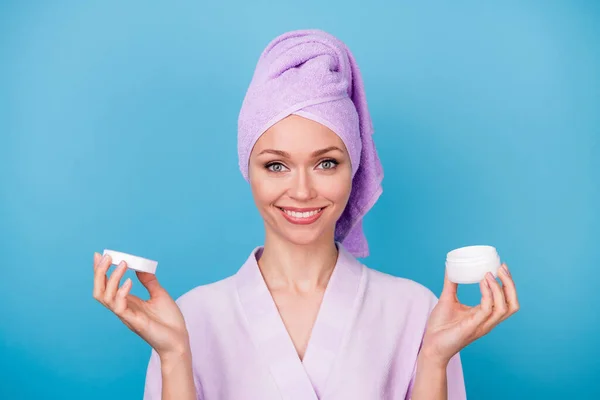 Foto de bonito jovem segurar frasco de bálsamo branco sorriso desgaste roxo toalha turbante banho roupão isolado azul cor fundo — Fotografia de Stock