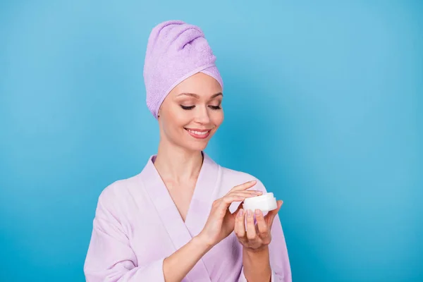 Foto de menina linda segurar frasco de bálsamo mão aplicar loção desgaste toalha violeta turbante roupão isolado azul cor de fundo — Fotografia de Stock