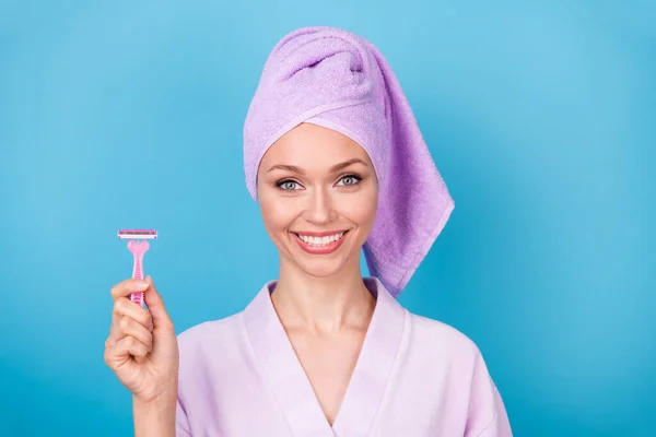Fénykép a csinos lány tartsa rózsaszín borotva penge sugárzó mosolygós viselet ibolya törölköző turbán fürdőköpeny elszigetelt kék szín háttér — Stock Fotó
