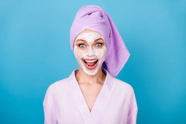 Φωτογραφία από κατάπληκτη μάσκα αφρού κυρία ανοιχτό στόμα λαμπερό χαμόγελο φορούν βιολετί πετσέτα τουρμπάνι μπουρνούζι απομονωμένο μπλε χρώμα φόντο — Φωτογραφία Αρχείου