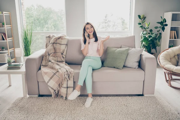 Фотопортрет молодой девушки, разговаривающей по мобильному телефону, сидящей дома на диване со скрещенными ногами — стоковое фото