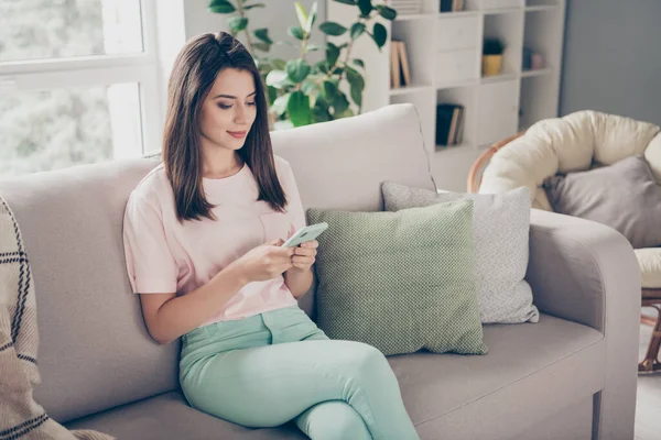Photo portrait of woman holding phone in two hands sitting on sofa with crossed legs indoors — Stock Photo, Image