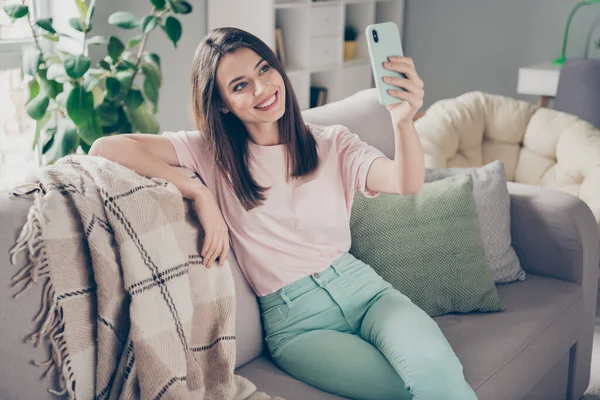 Foto portrét mladé dívky při selfie s mobilním telefonem sedí na gauči s nohama zkříženýma uvnitř — Stock fotografie