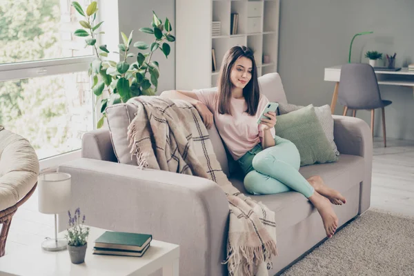 Фотопортрет мечтательной девушки с телефоном в одной руке, сидящей на диване в помещении — стоковое фото