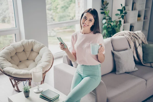 Photo portrait of happy young girl holding phone cup sitting on sofa arm relaxing indoors — Stock Photo, Image