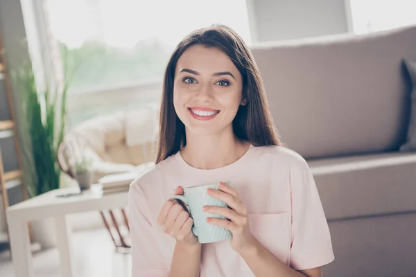 Foto retrato de mujer atractiva sosteniendo taza en dos manos sonriendo en el interior — Foto de Stock