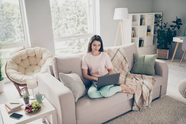 Фотопортрет женщины, сидящей на диване и смотрящей видео на ноутбуке в помещении — стоковое фото