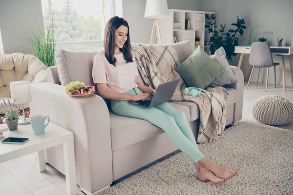 Фотопортрет молодой женщины, сидящей на диване с ноутбуком и улыбающейся в помещении — стоковое фото