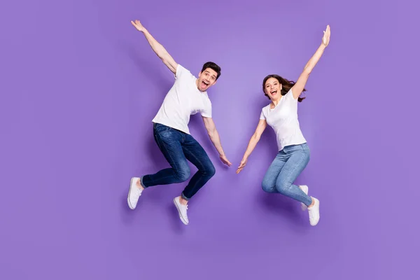 Volledige lengte foto van vrolijke getrouwde paar man vrouw springen genieten vrije tijd rust dragen casual stijl kleding sneakers geïsoleerd over violet kleur achtergrond — Stockfoto