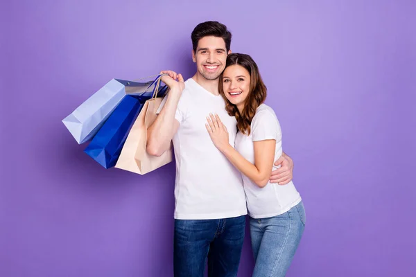 Photo joyeux jolie dame beau garçon couple de bonne humeur aller faire du shopping ensemble tenir de nombreux achats magasin paquet frénésie porter casual blanc t-shirts isolé violet fond de couleur pastel — Photo