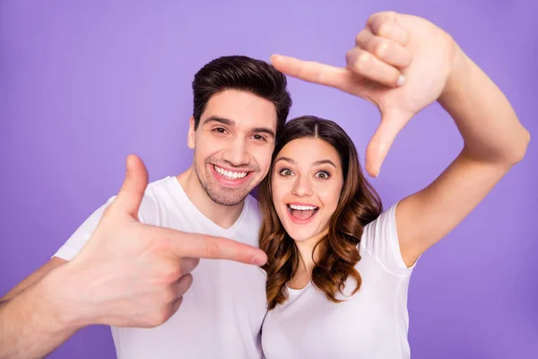 Retrato de cónyuges alegres positivos estudiantes hacen marco de dedo imaginar que viajan viaje fotografiando desgaste camiseta blanca aislada sobre fondo de color violeta —  Fotos de Stock