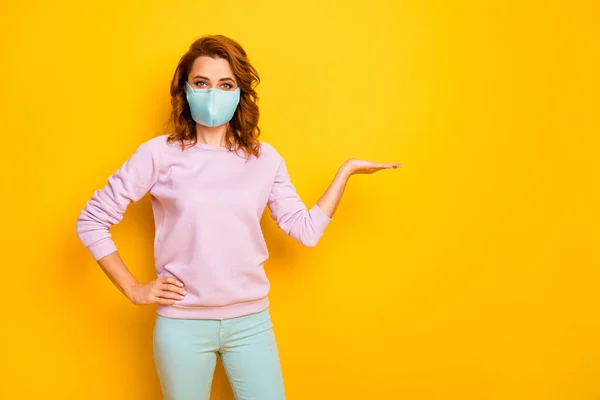 Foto de engraçado senhora positiva segurar espaço vazio palma aberta usar máscara rosa suéter verde calças isoladas cor amarela fundo — Fotografia de Stock