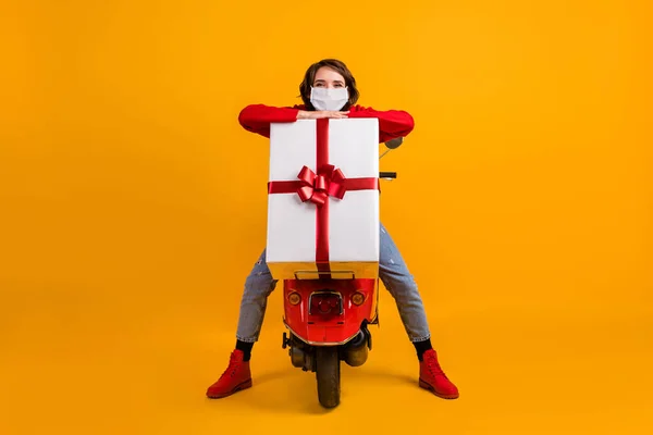 Full Size Foto von Mädchen sitzen roten Roller bekommen x-mas große Geschenkbox tragen Maske Pullover Jeans isoliert helle Farbe Hintergrund — Stockfoto