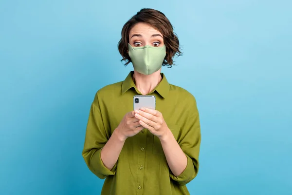 Foto de linda senhora bonito penteado curto segurar telefone olhar tela animado usar máscara verde camisa isolado azul cor de fundo — Fotografia de Stock